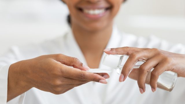 Cropped image of a smiling woman wearing a white robe putting micellar water on a cotton pad