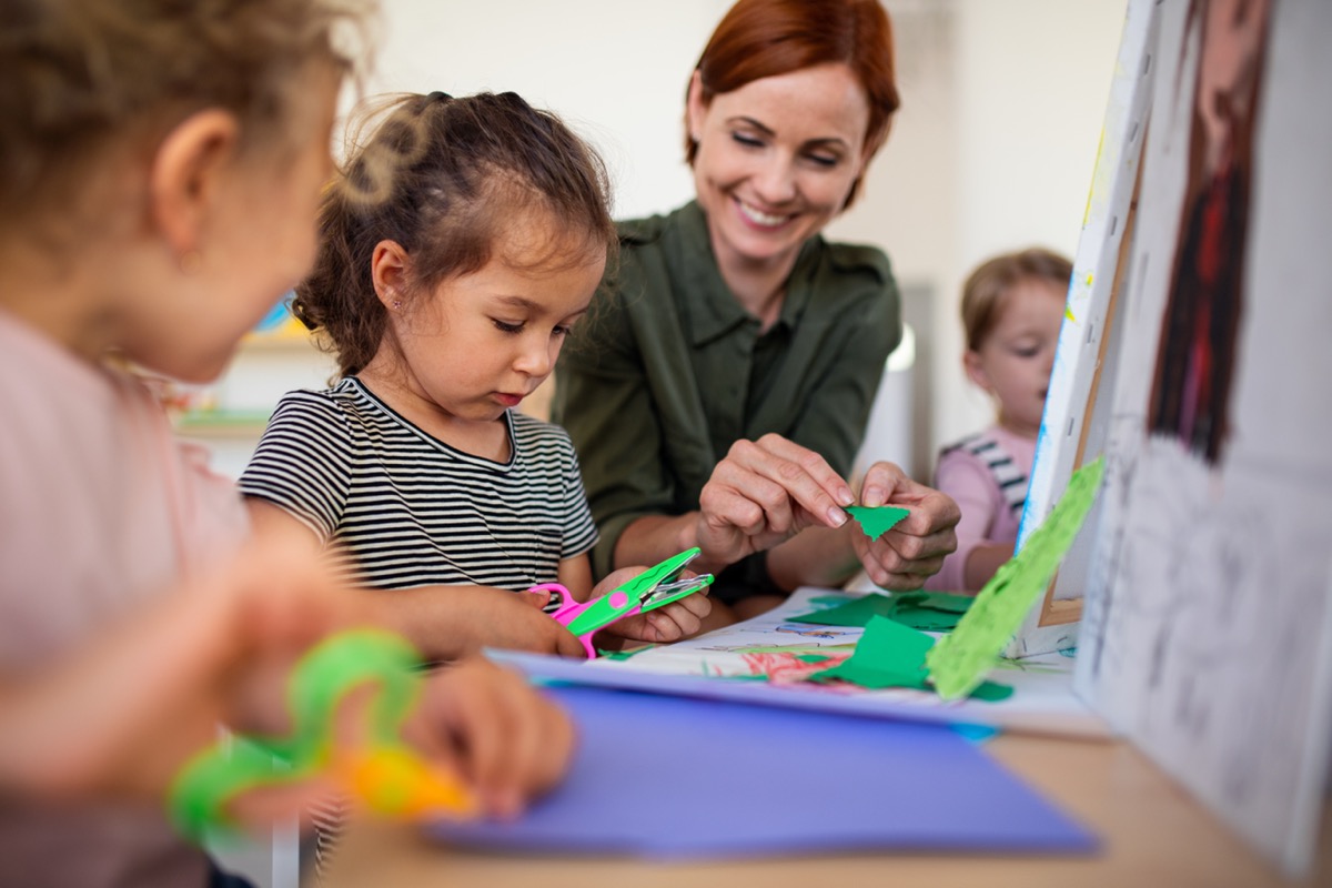 Group of small nursery school children with teacher in classroom doing arts and crafts
