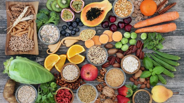 high-fiber foods on a wood table with fruit, vegetables, whole wheat pasta, legumes, cereals, nuts and seeds