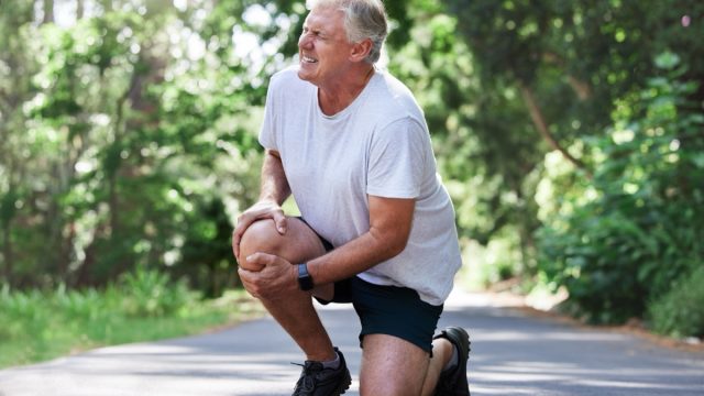 Running, injury and old man with knee pain on path in nature for outdoor fitness and workout exercise. Health, wellness and muscle strain, senior runner with hand on leg in support or relief for ache