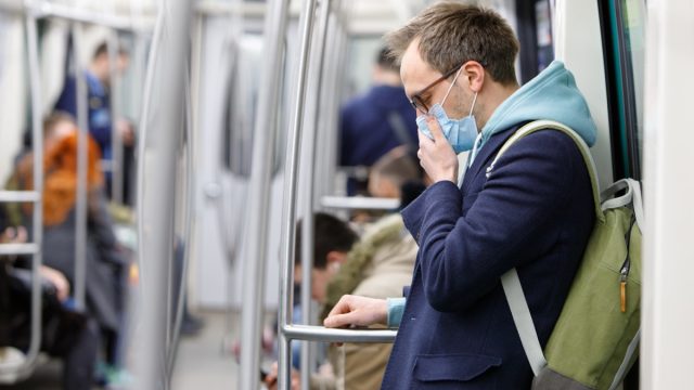 Ill man in glasses feeling sick, coughing, wearing protective mask against transmissible infectious diseases and as protection against the flu in public transport.