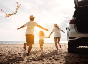 A family of three running on the beach next to their car
