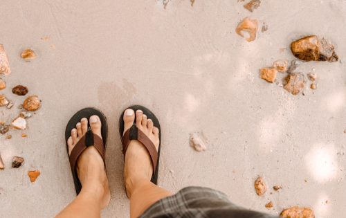Blurred man in Black slippers flip flop feet standing on the beach with a wave of foaming gentle beneath them.Top view