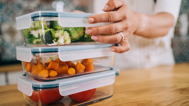 Close-up shot of female hands holding glass containers with fresh raw vegetables.