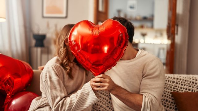 Man and woman kissing behind red hard balloon