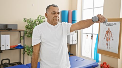 mature man exercising with dumbbell in rehabilitation clinic interior