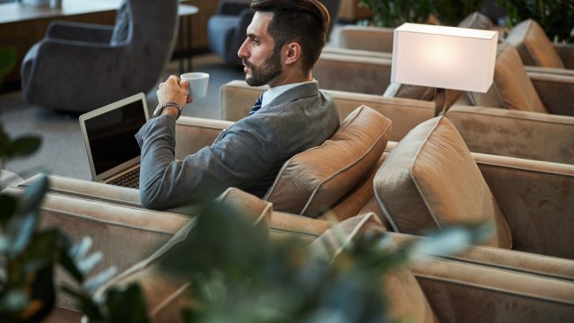 A man drinking coffee while working on a laptop in an airport lounge