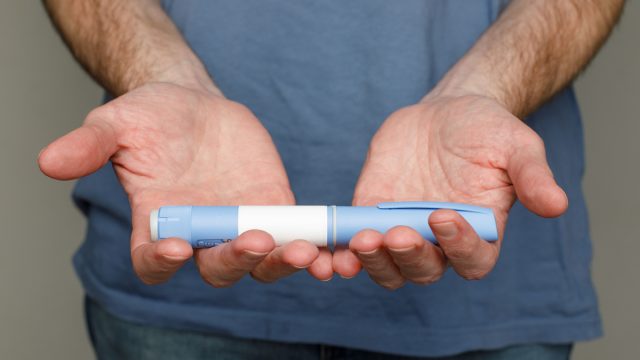 Close up of a man in a blue t-shirt holding out a Semaglutide or Ozempic pen