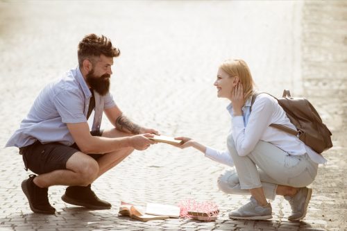 Man helping woman pick up books she just dropped on the street