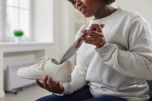 woman putting orthopedic insole into shoe. Close up shot of attractive woman in sweatshirt holding white leather sneaker. Foot care, prevention of flat feet and orthopedic diseases