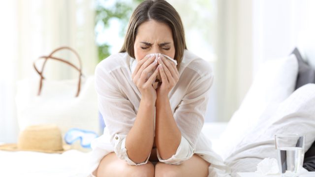 sick woman coughing in a hotel room while on a summer vacation