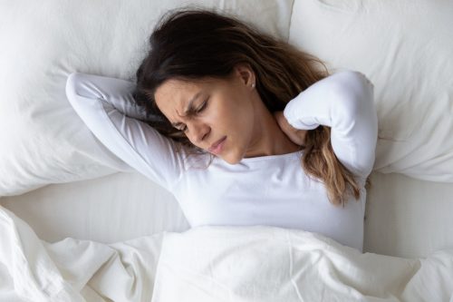 Top above view head shot close up stressed young mixed race woman feeling neck ache, suffering from painful feeling in neck in morning after sleeping on uncomfortable pillow at home or hotel room.