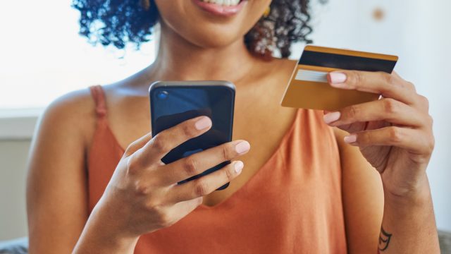 cropped portrait of a smiling woman wearing a rust-colored tank holding her iPhone and a credit card