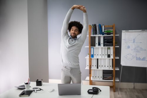 Young Businessman Doing Stretching Exercise In Office