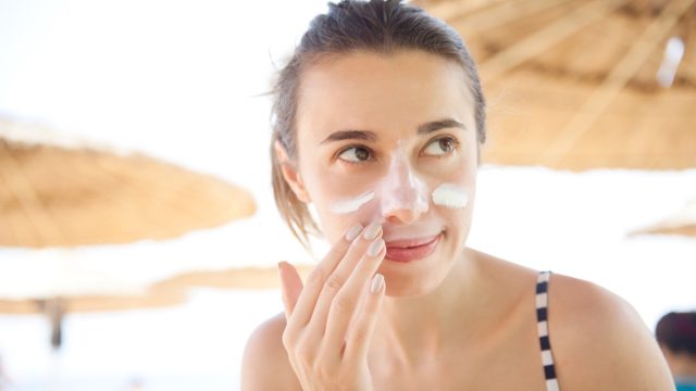 beautiful woman smears face sunscreen at the beach for protection.