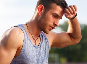 Tired athletic man wiping sweat from his forehead while outside