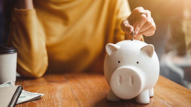 woman putting coins into a piggybank, demonstrating ways to save money each month