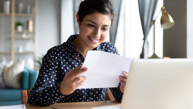 A woman smiling while reading a letter at her desk