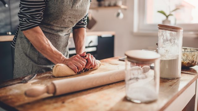 Woman standing in kitchen at a wooden countertop kneading dough