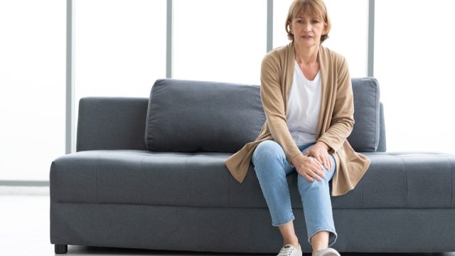 senior woman suffering from knee ache on sofa