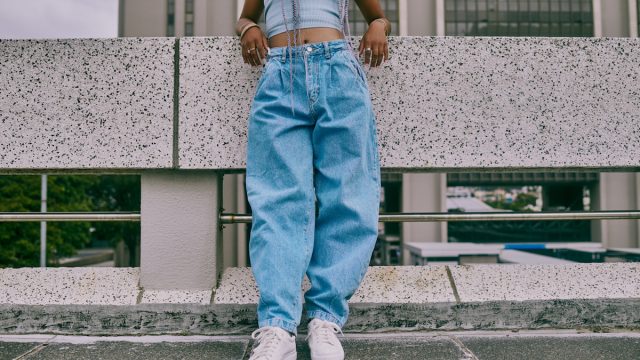 trendy woman in baggy jeans leaning on wall