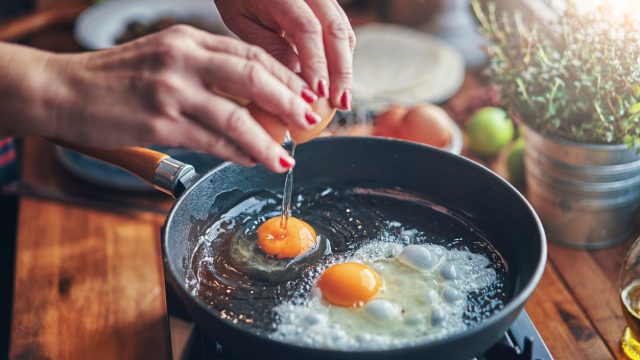 A close up of someone frying two eggs in a cast iron skillet