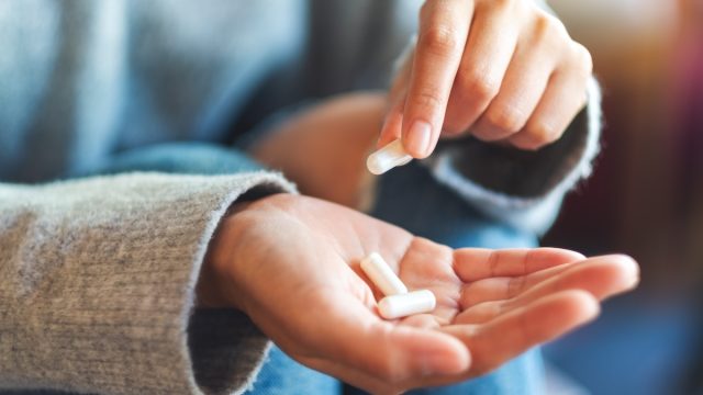 Closeup image of a woman holding and picking white medicine capsules in hand