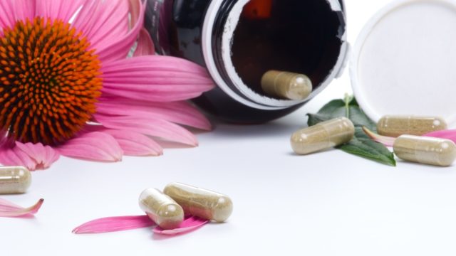 Closeup of Echinacea extract pills and fresh Echinacea flowers on white background