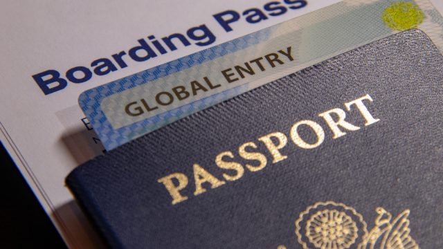 A close up of a passport with a Global Entry card in it sitting on a boarding pass