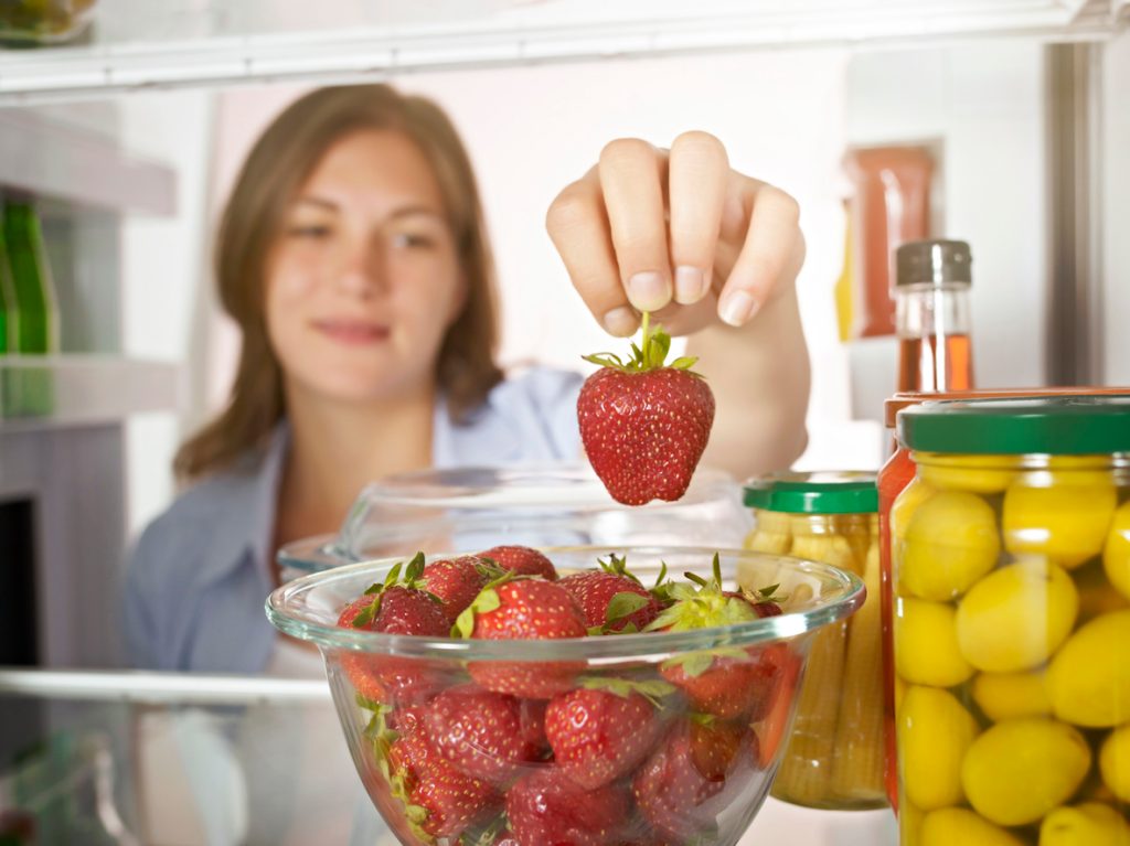 A woman taking a strawberry out of the fridge