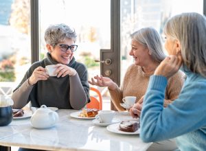 Group of mature women having fun during breakfast while drinking coffee and eating cake