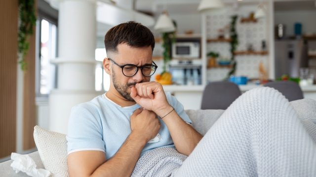Sick man holding his chest in pain while coughing in the living room.