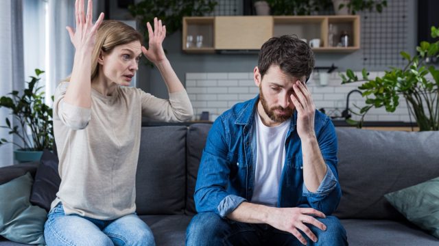 Family quarrel, man and woman sitting on sofa at home. angry woman yells at her husband, blames. The man is silent. He listens, holds his head, embarrassed