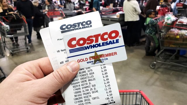 A hand holding a receipt and Costco Membership card in Costco warehouse. Costco is an American corporation which operates a chain of membership only warehouses.