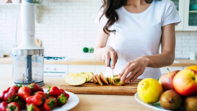 Woman cutting up an apple on a cutting board with other fruit on her kitchen counter