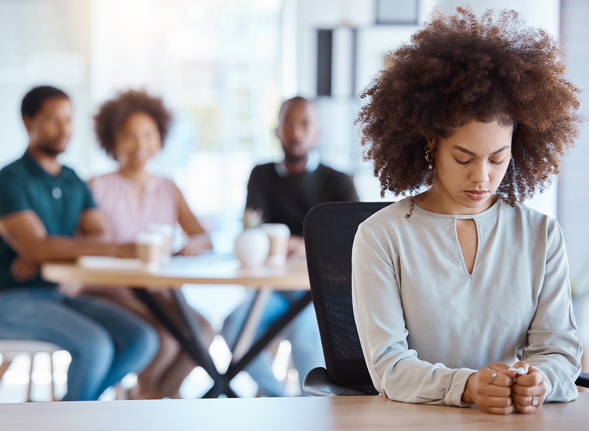 A woman looking lonely at work with colleagues in the background