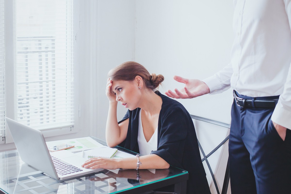 A woman looks upset as her boss stands over her