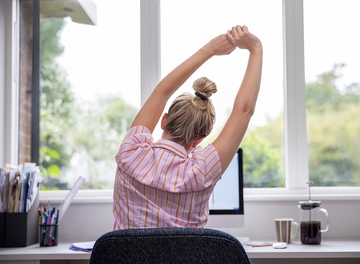 A woman stretches at her desk after prolonged sitting while working