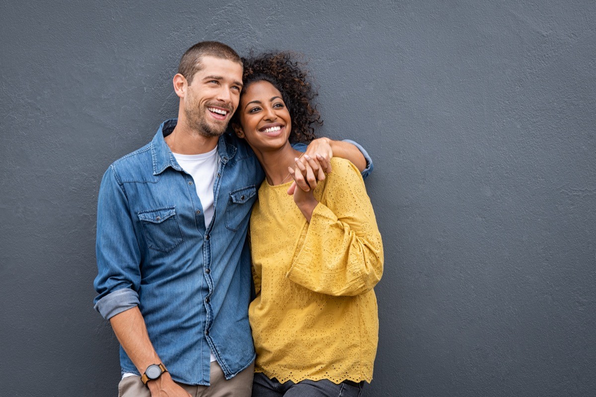 Happy couple hugging against a gray wall