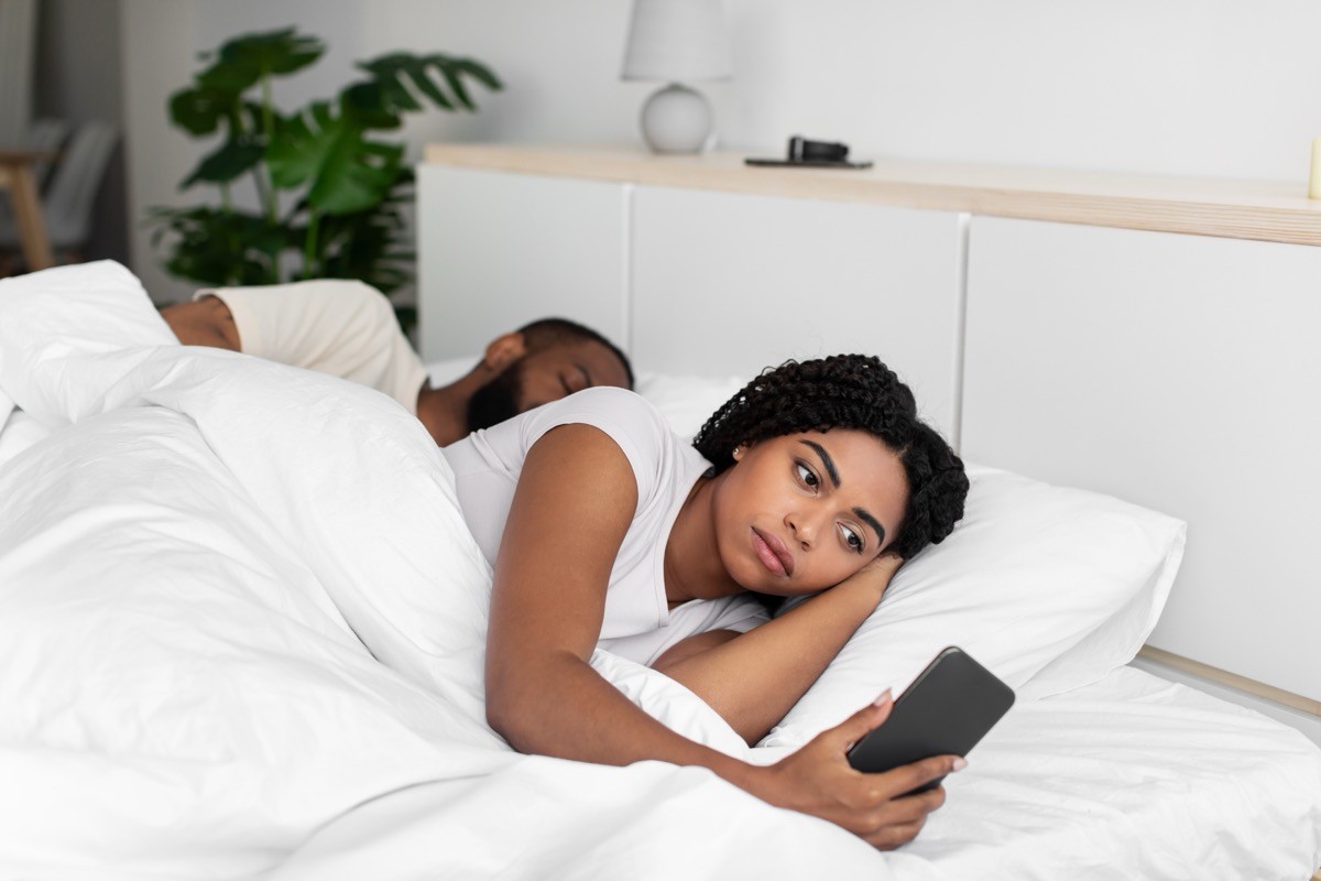 woman being secretive with her phone while lying in bed