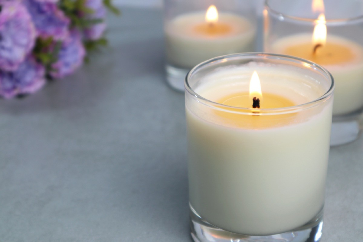 Close-up of candle in glass container burning with two candles behind it