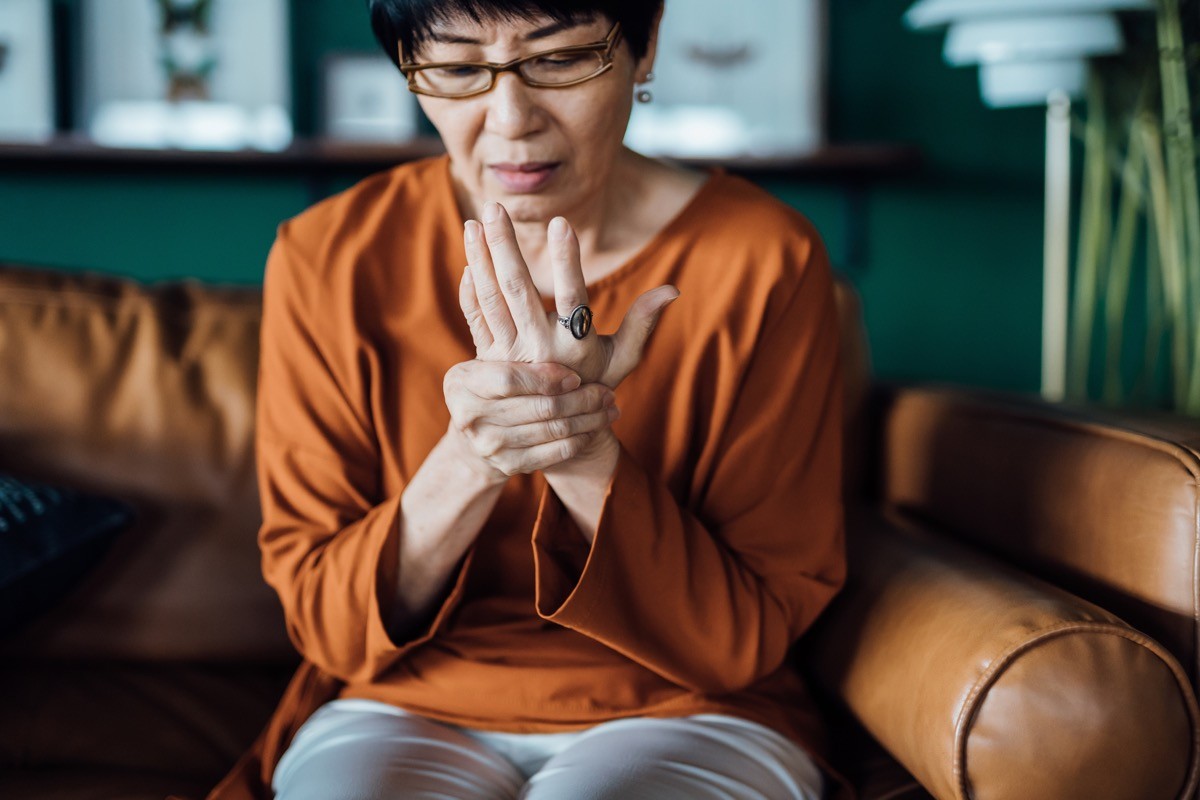 woman rubbing her hands in discomfort, suffering from arthritis in her hand while sitting on sofa at home.