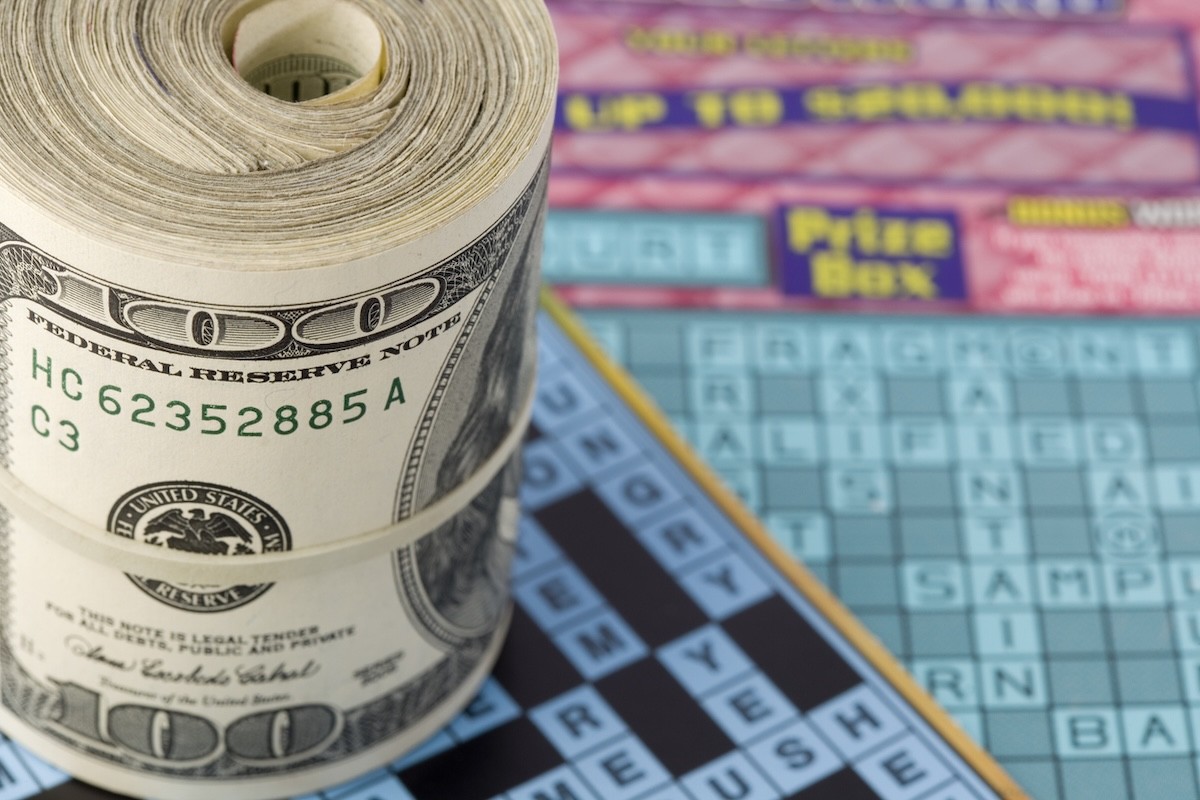 roll of $100 bills sitting on scratch-off lottery tickets