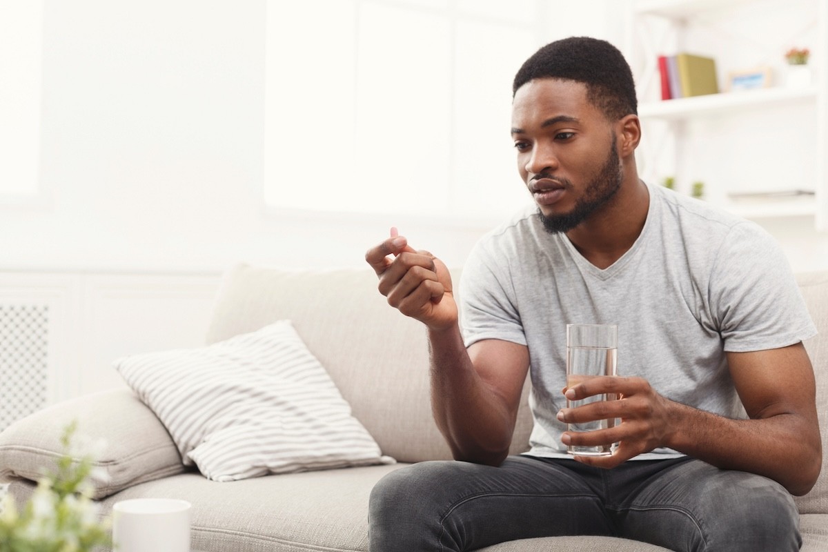 man on couch about to take a vitamin or supplement with a glass of water
