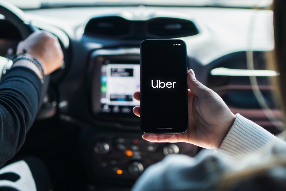 A person looking at their phone with the Uber logo on the screen while riding in a car