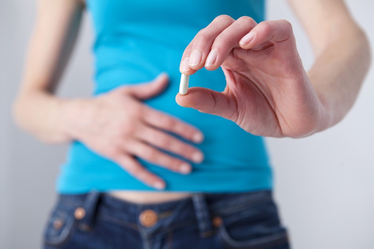 woman holding probiotic supplement with her hand on her stomach