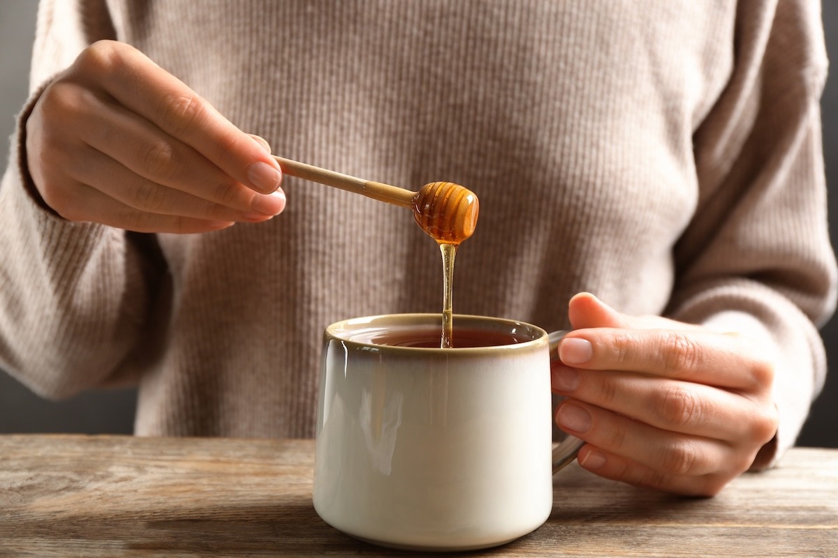 closeup of a woman adding honey to a mug of tea