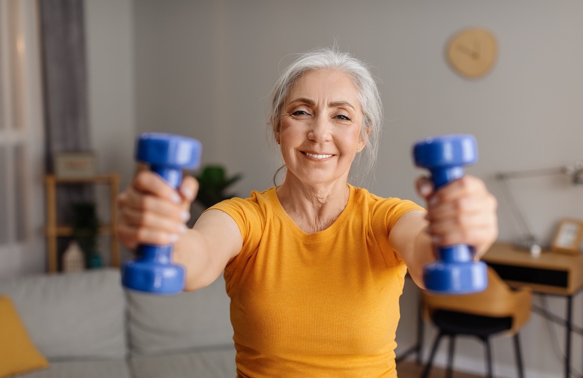 mature woman in a yellow t-shirt raising blue free weights