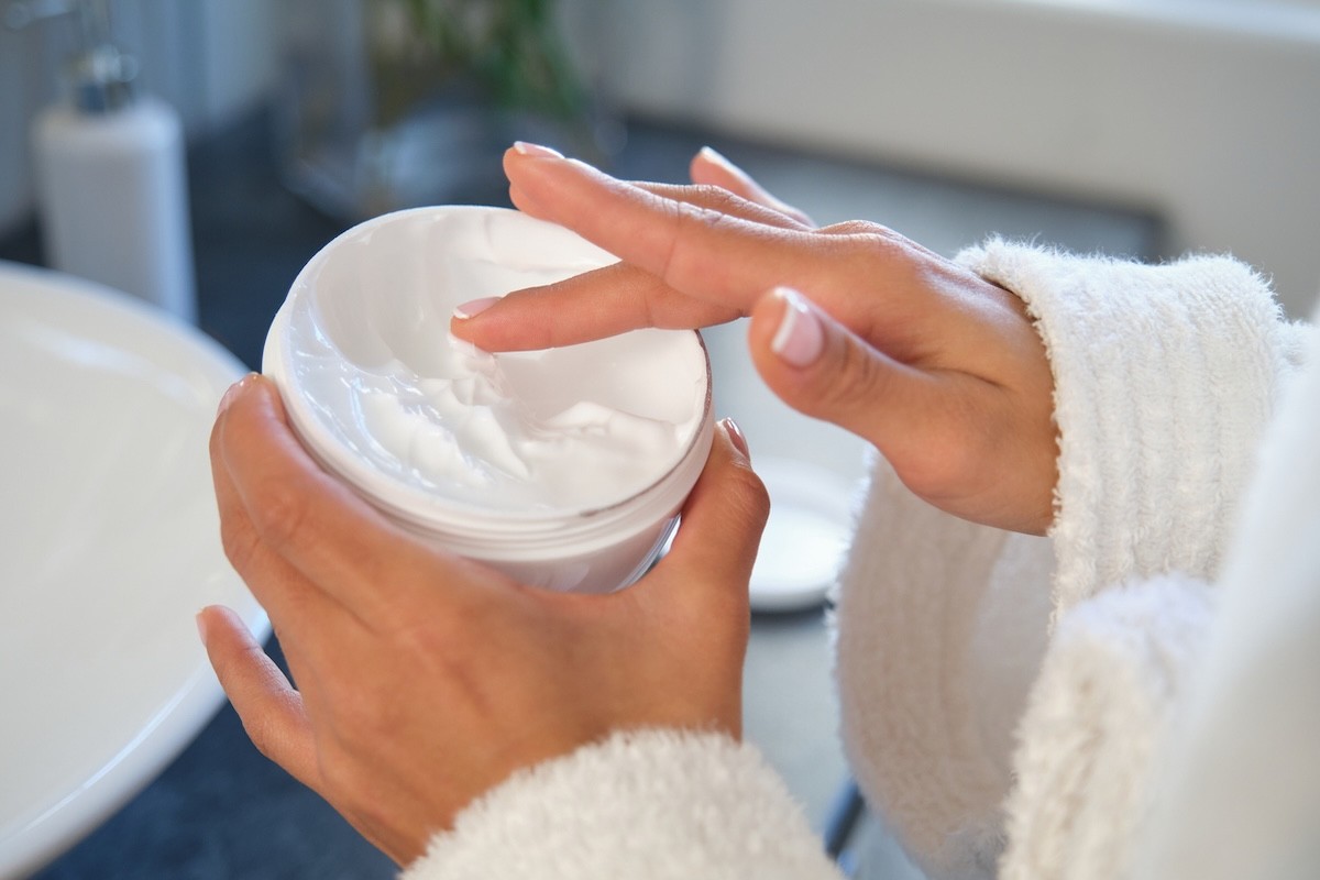 closeup cropped image of a woman dipping her hand into a tub of white body cream