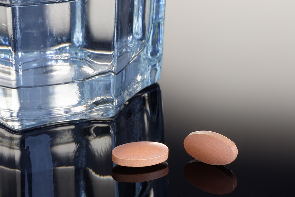two pills sitting next to a glass of water